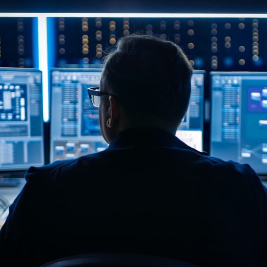 a man sits in front of many computer monitors. he is securing the cyber.